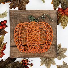 an orange string pumpkin sitting on top of a wooden board surrounded by leaves and berries