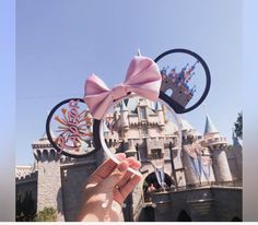 a hand holding up a minnie mouse ears with a castle in the background