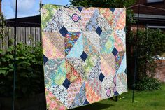 a patchwork quilt hanging on a clothesline in front of a brick wall and green grass