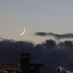 the moon is shining in the sky above some buildings and clouds at night time,