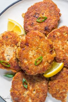 several crab cakes on a plate with lemon wedges