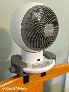 a white and gray fan sitting on top of a wooden table next to a wall