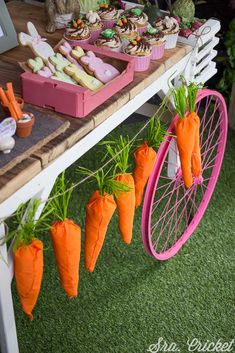 some carrots are hanging from a pink bike wheel on the grass near other food items