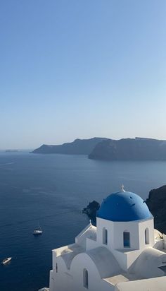 a white and blue church on the edge of a cliff overlooking the ocean with boats in the water