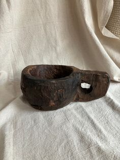 an old wooden bowl sitting on top of a white cloth covered tablecloth with a hole in the middle