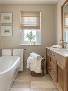 a white bath tub sitting next to a bathroom sink under a window with roman shades