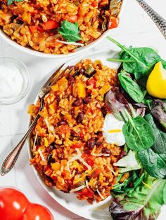 two plates filled with rice and vegetables on top of a white table next to some lemons