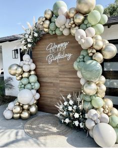 an arch made out of balloons and greenery with the words happy birthday written on it