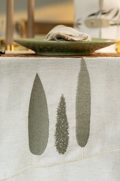 the table cloth has three trees on it and is next to a plate with a napkin