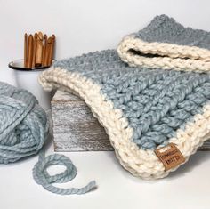 a crocheted blanket sitting on top of a wooden box next to some knitting needles