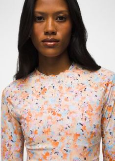 a woman with long black hair wearing an orange and blue floral shirt, standing in front of a white background