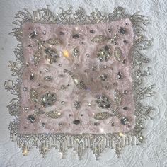 a pink square with silver sequins and beads on a white lace tablecloth