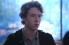 a young man with curly hair is looking at the camera while sitting in front of a television screen