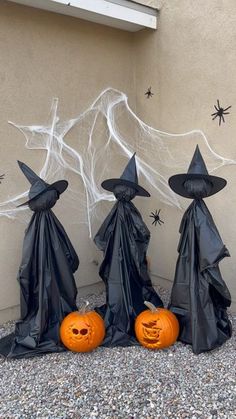 three black plastic witches with pumpkins in front of a wall decorated for halloween time