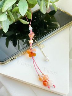 a cell phone is sitting next to a plant with beads and pearls hanging from it