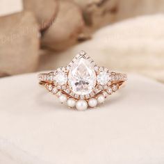 an engagement ring with a pear shaped diamond surrounded by small white pearls on a bed