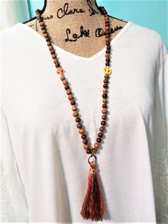 long silk tassel necklace. wooden bead necklace for women.  brown beaded tassel necklace. orange. fall. tassel. handmade tassel necklace  Naturalistic lightweight fall season boho necklace.   My beaded fringe tassel necklace is 32 inches long with a 4 inch long multi colored tassel.  Nice for Summer thru October. Tassel is silk threads in the colors of orange, soft yellow, olive green, pale peach and brown.   Hangs by a bronze ring to the necklace. All brown hues of wooden beads spaced by gold metallic Toho glass beads.   A yellow peace symbol and orange cross adorn the necklace also. A "Made with Love" Charm is on the back. Closure is a bronze lobster claw hook. All handmade in my beading shop. Gift for a friend, sister, aunt or mother.  You receive the item pictured here as I do not make Handmade Adjustable Brown Tassel Necklace, Brown Tassel Necklaces As Gifts, Adjustable Bohemian Jewelry For Fall, Bohemian Adjustable Jewelry For Fall, Bohemian Tassel Necklace With Wooden Beads For Gift, Bohemian Wooden Beads Tassel Necklace Gift, Handmade Bohemian Jewelry For Fall, Silk Tassel Necklace, Wooden Bead Necklace