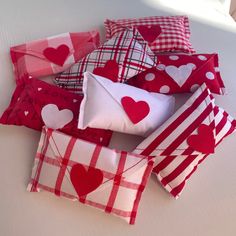 several pillows with hearts on them sitting on a bed together, one is red and the other is white