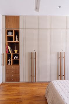 a bed sitting in a bedroom next to a wooden shelf filled with books and vases