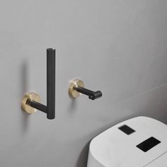 two black and gold handles on a gray wall next to a white trashcan with a toilet paper dispenser