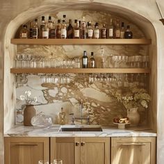 a kitchen filled with lots of bottles and glasses on top of a wooden shelf next to a sink