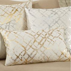 three white and gold pillows sitting on top of a couch next to a pillow case