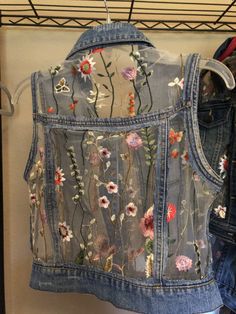 a jean jacket with flowers on it hanging from a rack