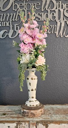 a vase filled with pink flowers sitting on top of a wooden table next to a wall