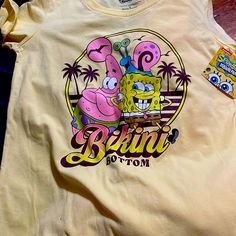 Spongebob And Patrick Bikini Bottom T-Shirt Beach Cotton Top With Character Print, Summer Vacation Tops With Character Print, Cotton Character Print Beach Top, Cotton Beach Top With Character Print, Cotton Character Print Tops For Beach, Cotton Cartoon Print Top For Beach, Short Sleeve Tops With Character Print For Vacation, Fun Cartoon Print Tops For Vacation, Yellow Graphic Print Top For Beach Season