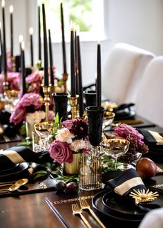 the table is set with black and gold place settings, flowers, candles, and fruit