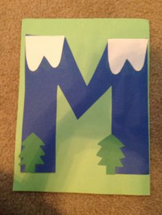 a paper cut out of the letter m with mountains and trees on it's sides