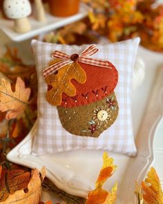 a white plate topped with a pillow covered in fall leaves and an acorn decoration