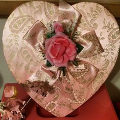 a heart shaped box with a pink rose in it on top of a red table