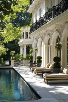 an outdoor swimming pool with chaise lounges and potted trees in the background