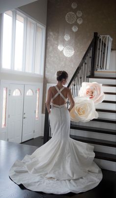 a woman in a wedding dress is walking down the stairs with flowers behind her back