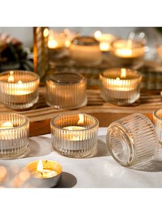 candles are lit on a table with plates and bowls in the foreground, surrounded by other glass objects