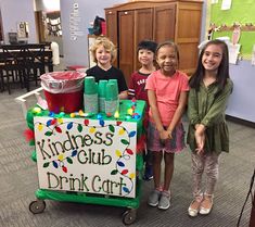 three children standing next to a sign that says kindness club drink cart on it in an office