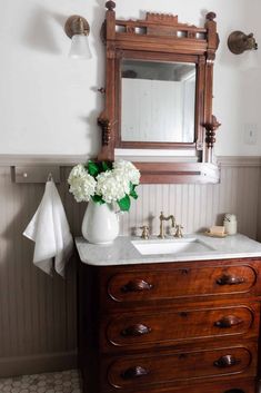 a bathroom with a sink, mirror and flowers on the dresser in front of it