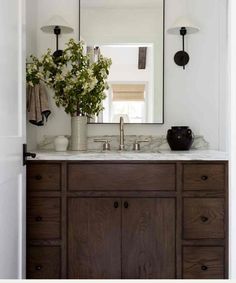 a bathroom vanity with a large mirror above it and flowers in the vase on top