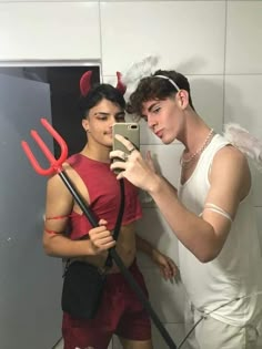 two men dressed up in devil costumes are taking a selfie with their cell phone