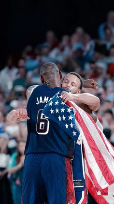 two men hugging each other while holding an american flag in front of them and people watching from the stands