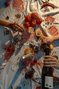 two hands holding a bottle and some food on a table with other items around it