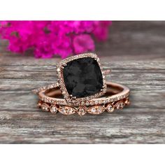 a black diamond ring set on top of a wooden table with pink flowers in the background