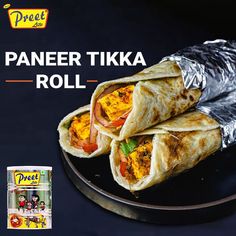 a paneer tika roll on a black plate with foil wrapper over it