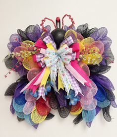 a multicolored mesh wreath hanging on the wall with a black vase in it