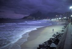 a person walking on the beach at night with lights in the sky and dark clouds