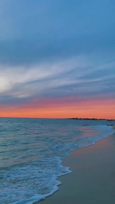 a beach with waves coming in to shore and the sun setting on the horizon behind it