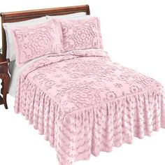 a bed with pink bedspread and pillows on top of it, next to a night stand