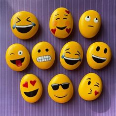 nine yellow smiley face rocks with hearts and sunglasses painted on them, sitting on a purple surface