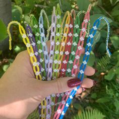 a hand holding several different colored bracelets in it's palm, with green leaves behind them